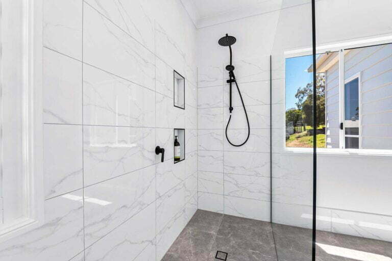 Spacious Master Bathroom Walk-in Shower with twin heads, floor and wall tiles, black fixtures on neutral tones, glass shower screen and niche wall storage