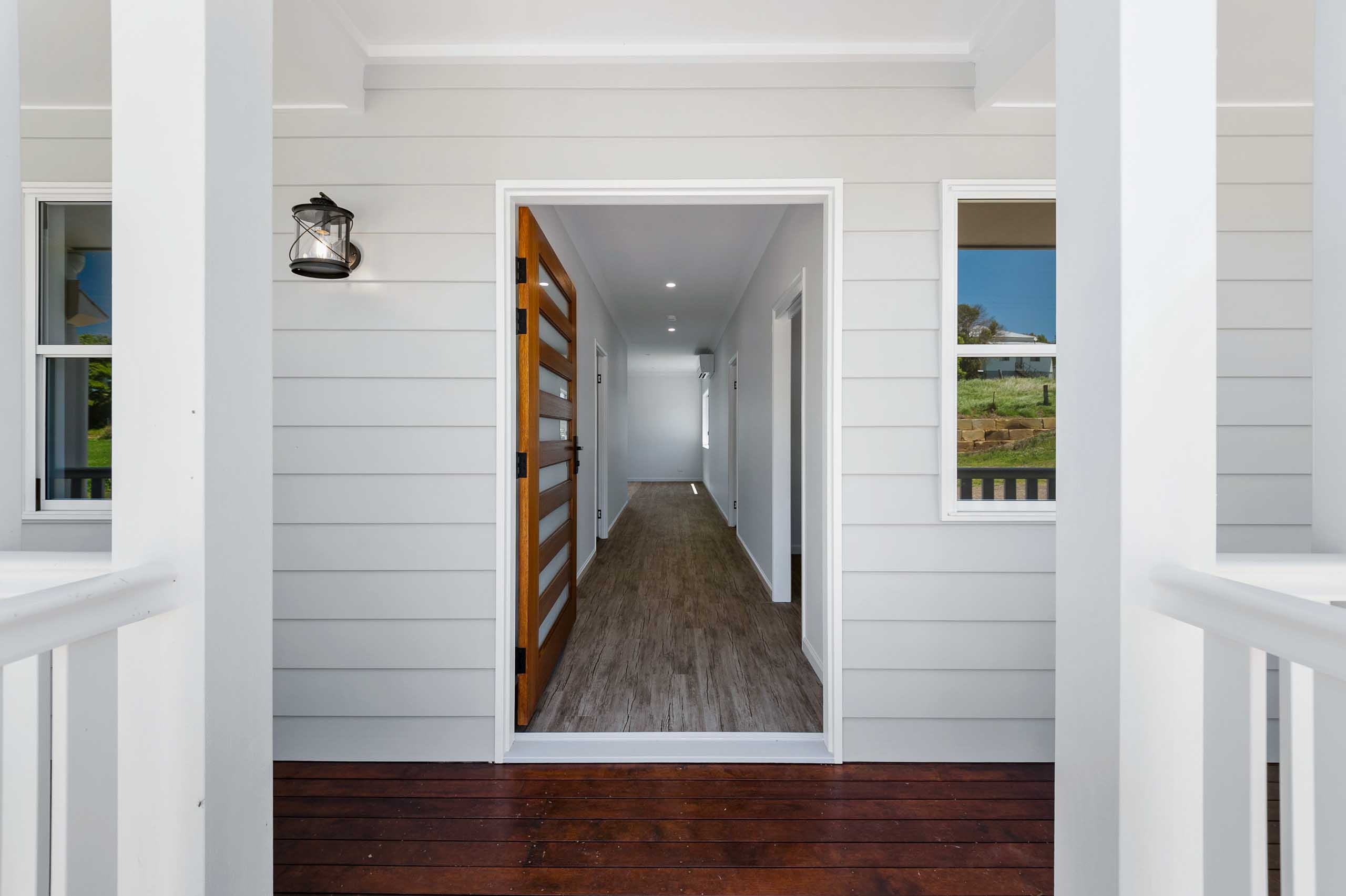 Front Entry to a modern colonial home in Killarney Hills, Qld. Build materials are mostly timber and linear board and colours are neutral with darker timber decking and an extra wide door to create contrast between the textures and surfaces.